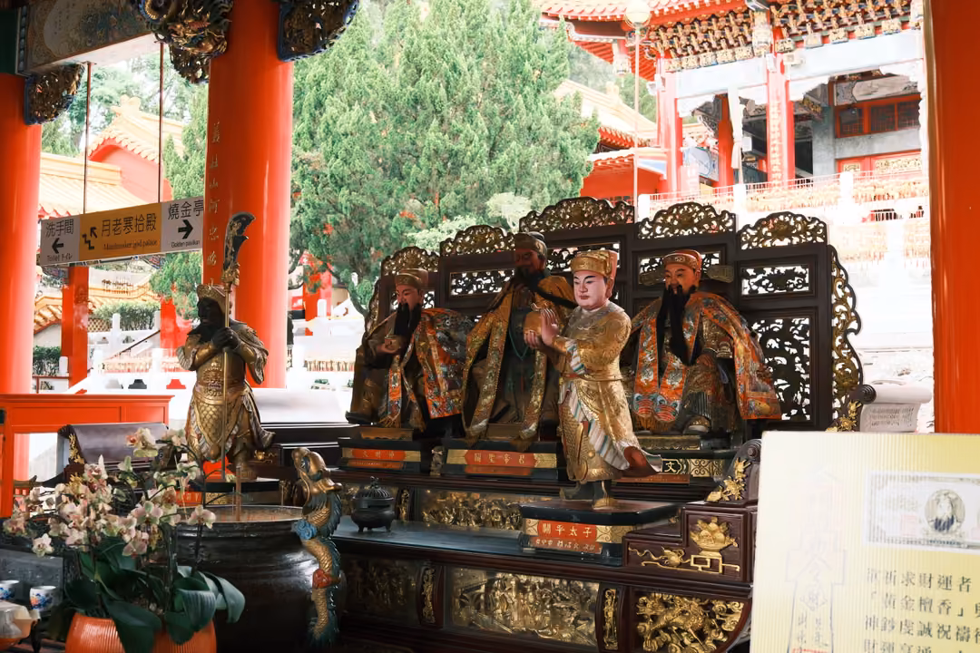 Altar of painted figures seated before a carved screen with orchids, red pillars and a courtyard beyond