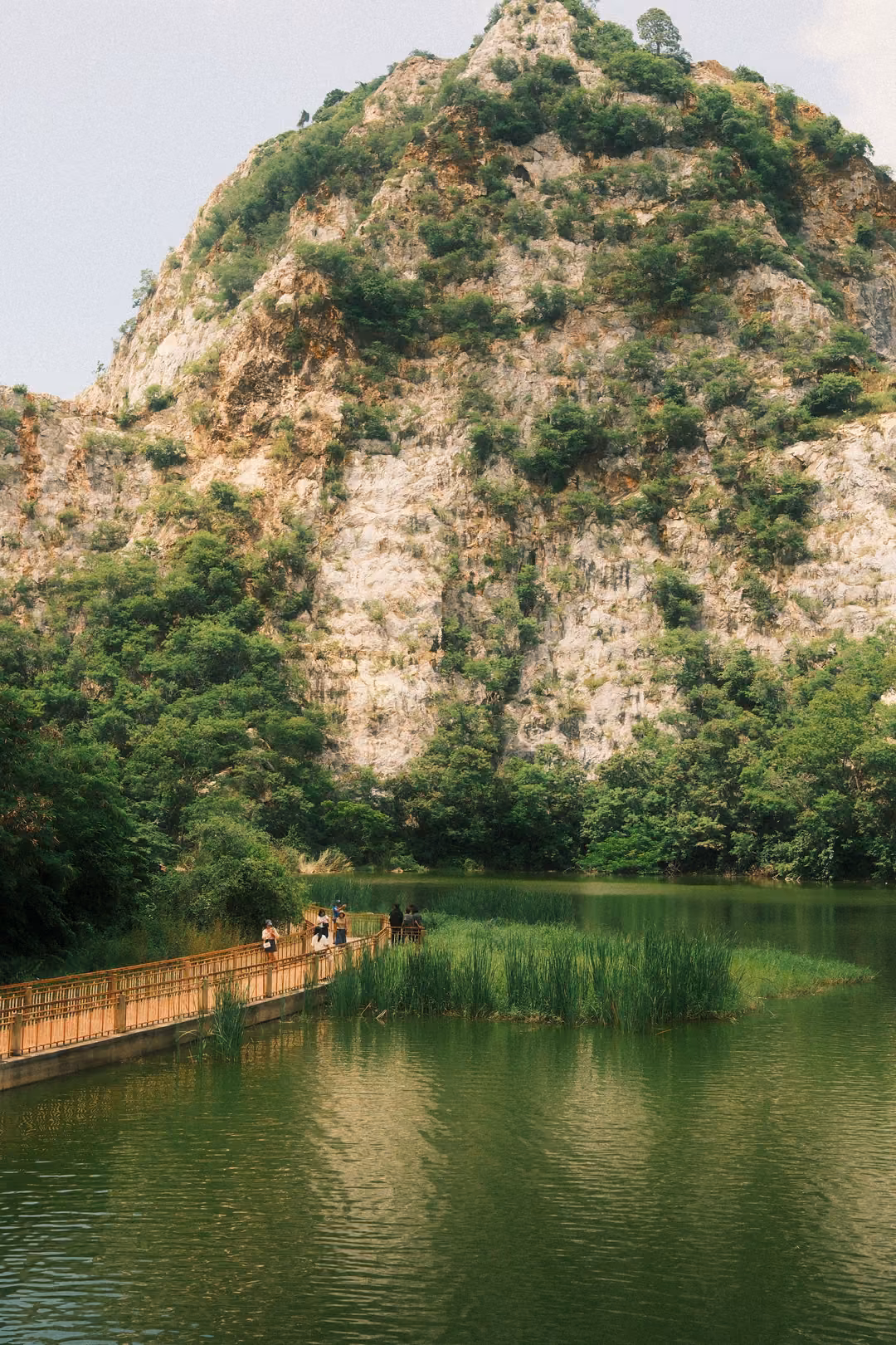 Tall limestone peak above a lake, a wooden boardwalk with railings stretching across the water with people on it