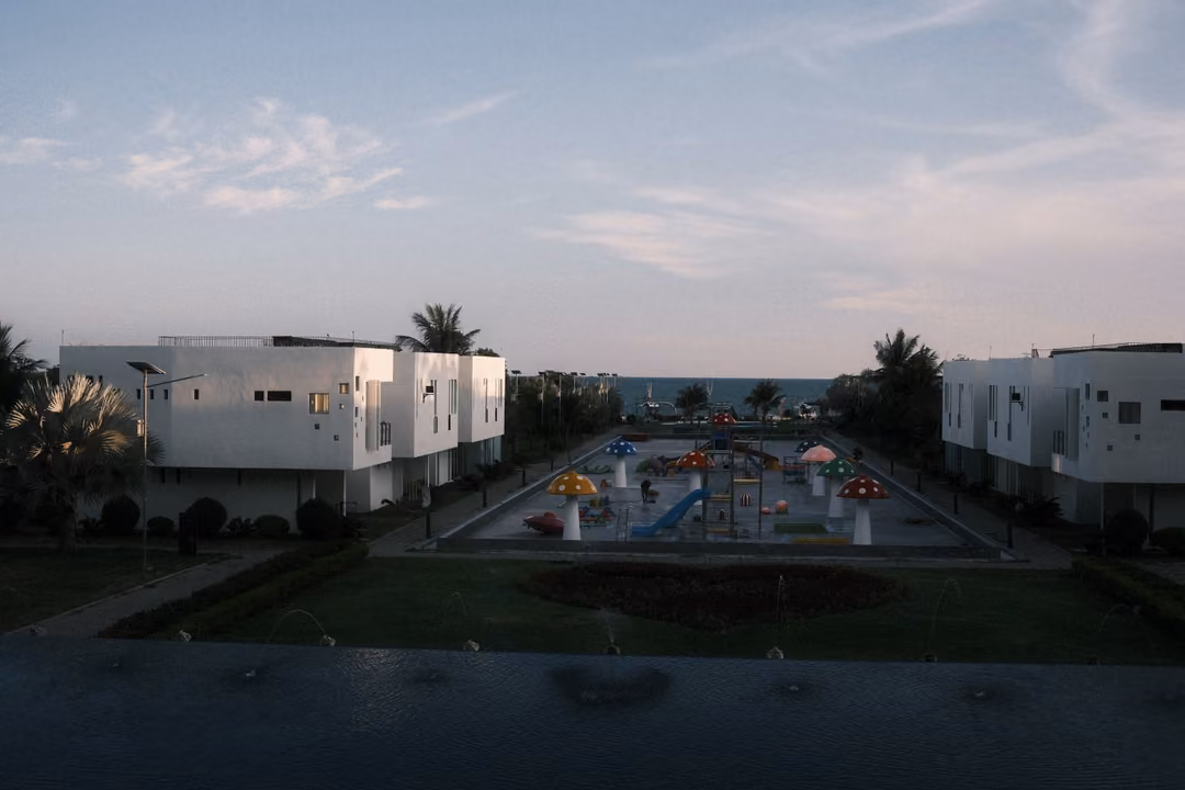 Dusk view of white villas and a splash park with colourful umbrellas, a dark pool in the foreground