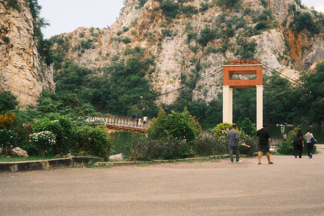 Paved area beneath limestone cliffs, a red and white gateway tower and a few visitors walking toward it