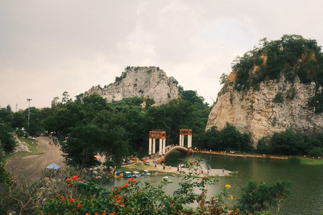High view over a lake with a suspension bridge and red and white towers, rounded limestone crags and flowering shrubs