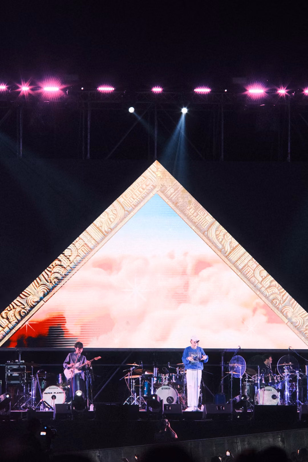 Vertical view of a gold-framed triangle filled with pink clouds, the singer and guitarist on stage below.