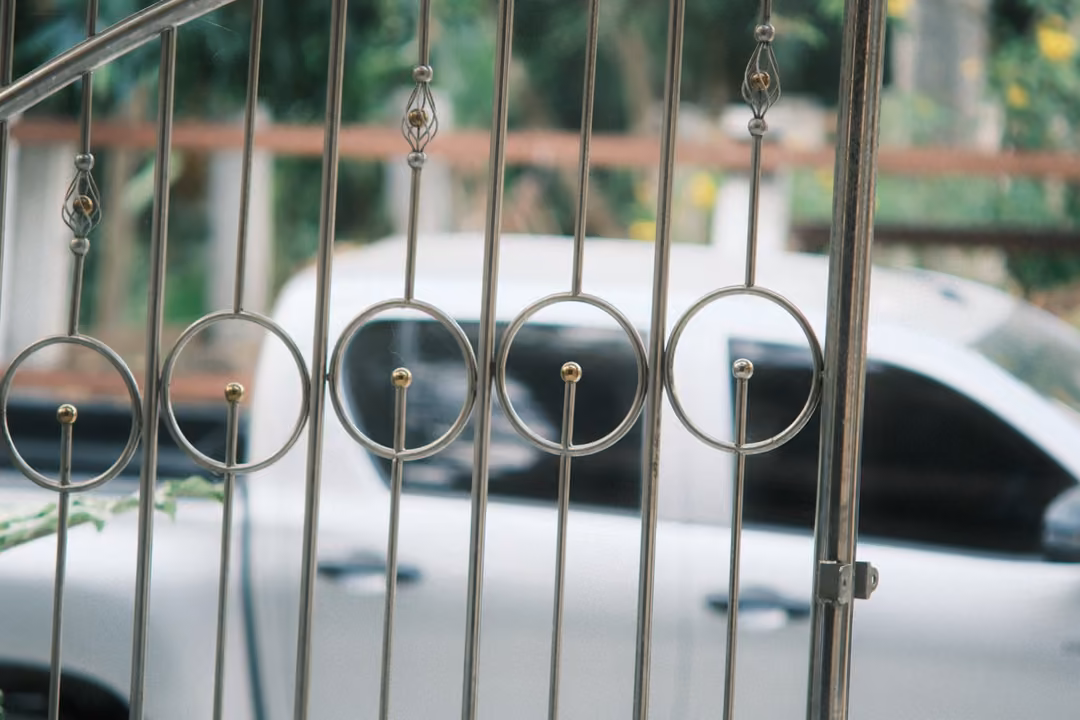 White pickup truck seen through ornate silver metal gate bars with circular details