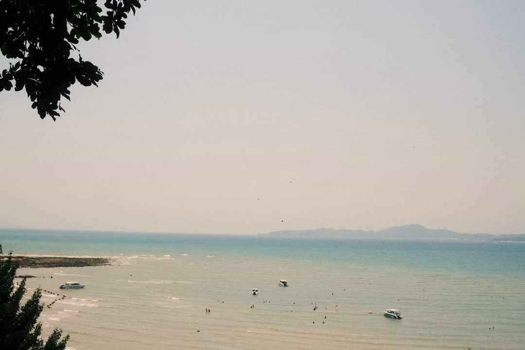 Hazy turquoise sea with a few boats and swimmers, a pale sky and a faint island on the horizon