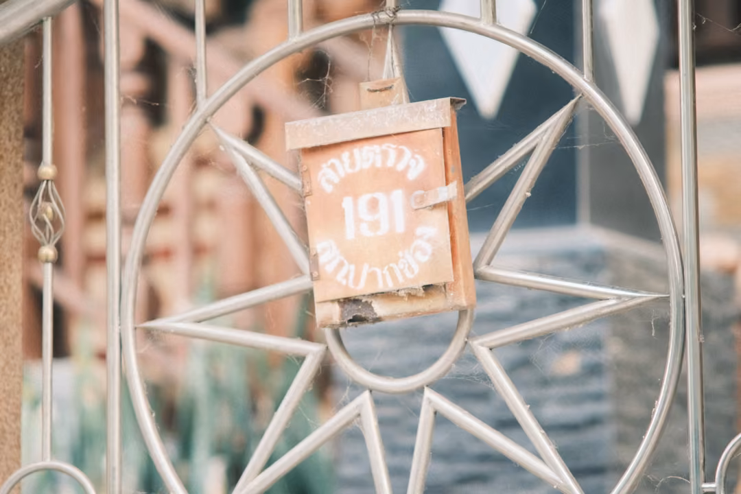 A rusted mailbox marked 191 hung on a metal gate with a large star-shaped ornament, a wooden house behind.