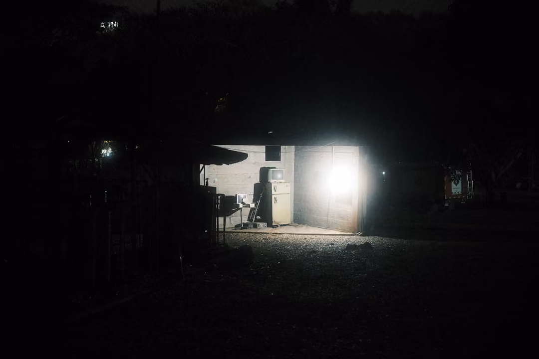 Dark night scene with a single lit garage or room glowing white in the distance