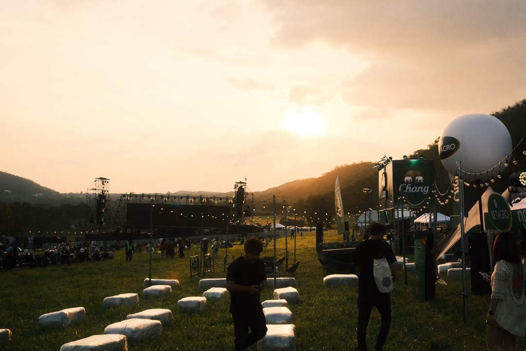 White bales on grass with silhouetted people walking past, a large white balloon and a banner behind.