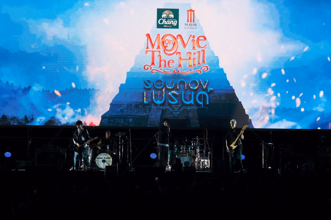 Screen showing the Movie on The Hill title over a pyramid and clouds, three musicians on the dim stage below.
