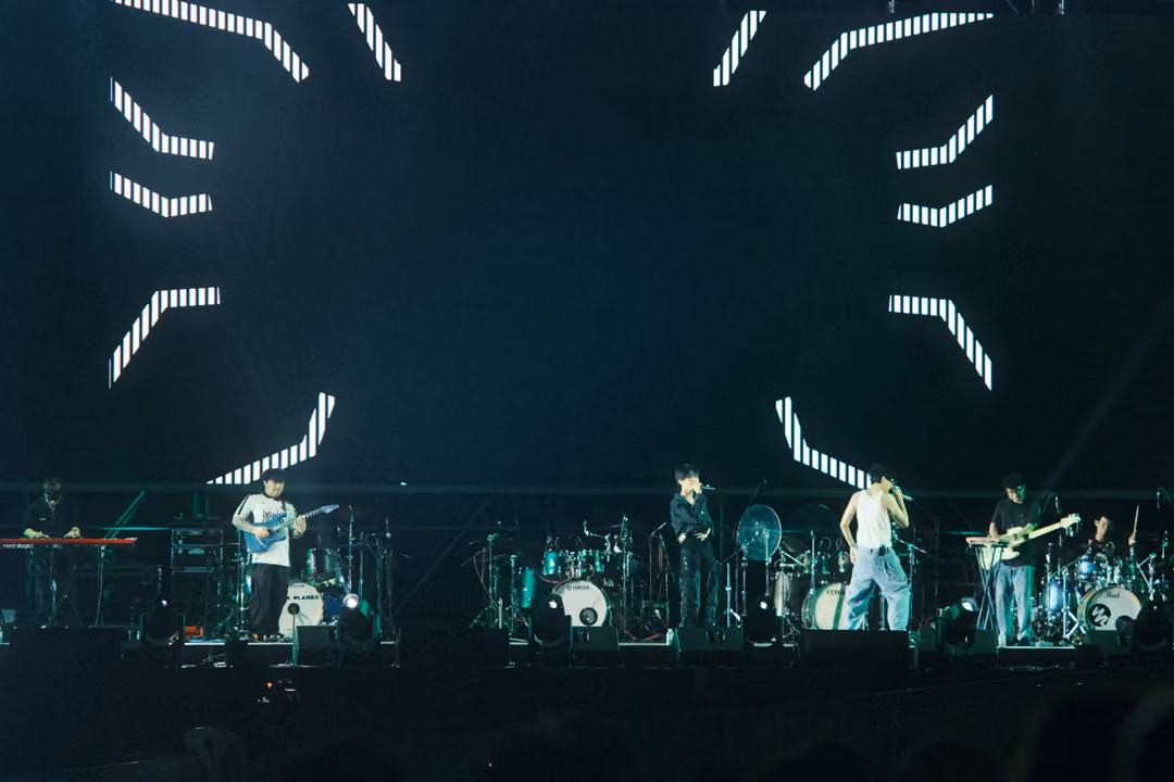 Band on stage below a dark screen with white dotted branching lines appearing from the edges.