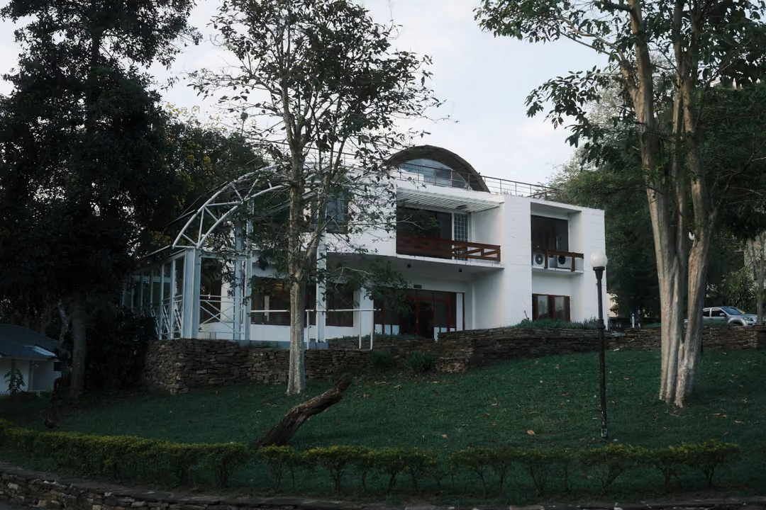 White modern building with an arched glass roof, balconies and a green lawn with trees