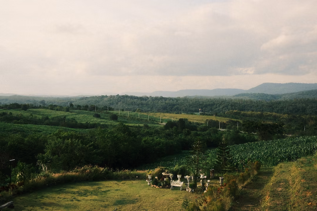 A wide view of a green valley under a cloudy sky, distant mountains and a lawn with white figures below.