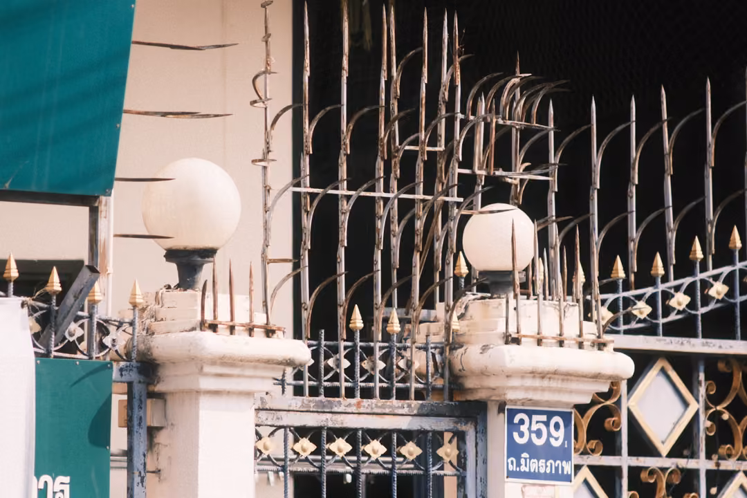 A spiked iron gate with gold tips, white globe lamps on pillars and a blue house number plate reading 359.