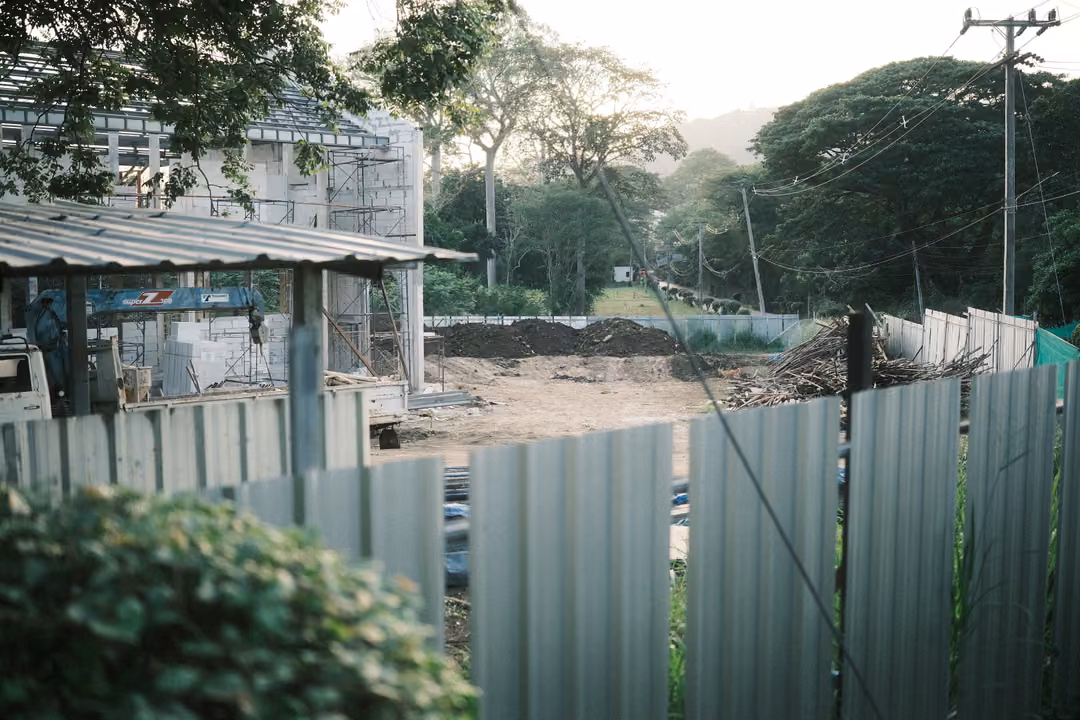 Construction site behind metal fencing with an unfinished building, trees and power lines