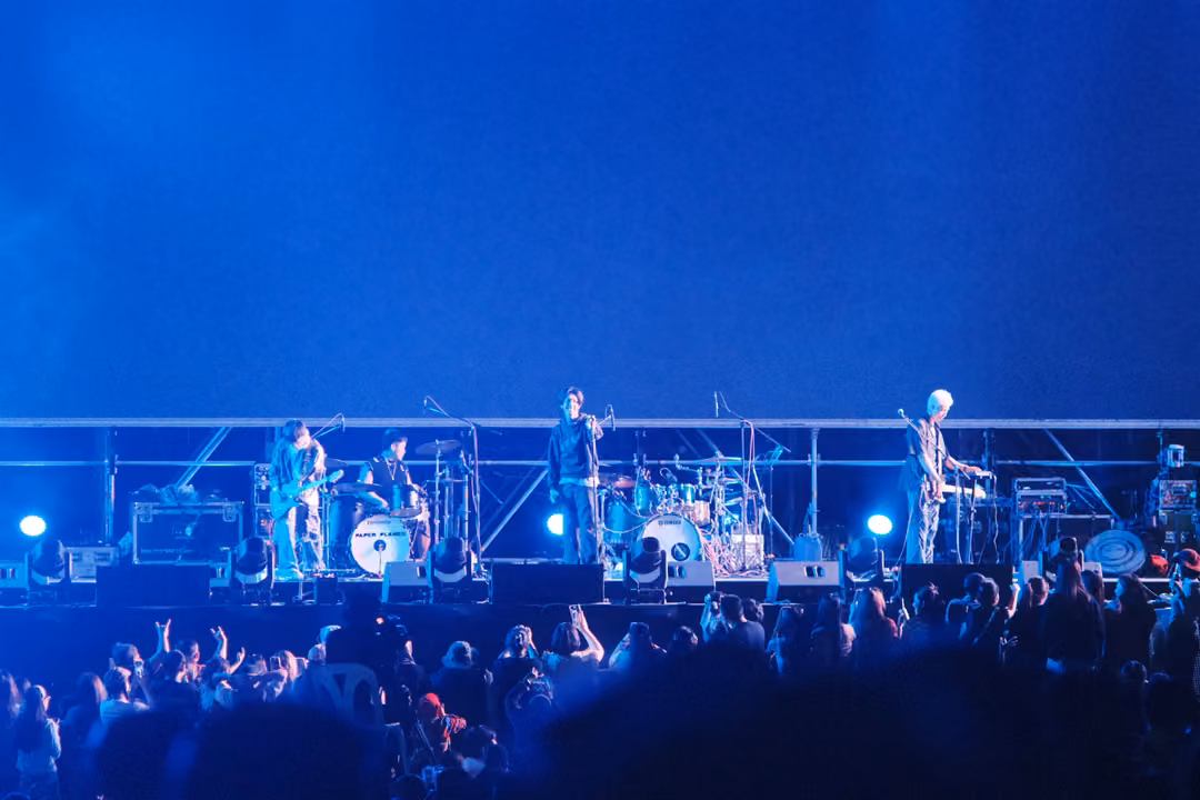 Band on stage under a deep blue empty screen, crowd in the foreground lit blue.