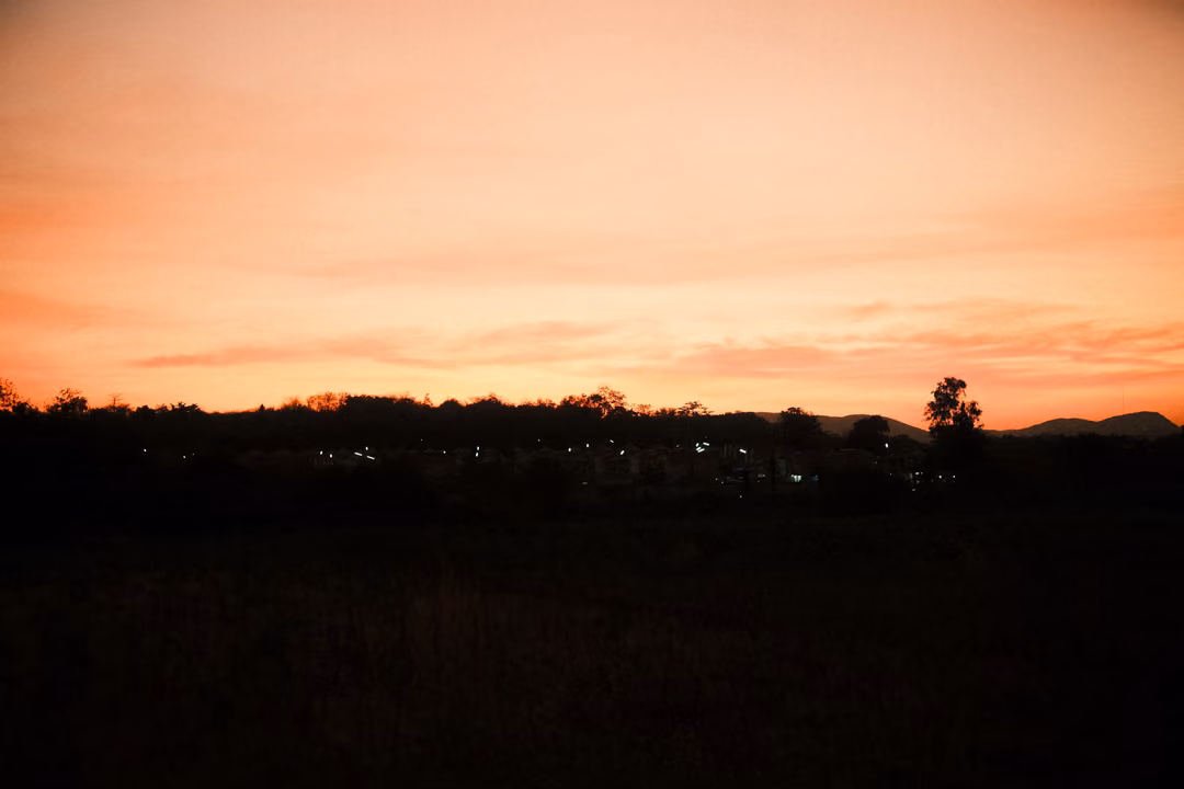 Deep orange sky streaked with clouds above a dark silhouetted horizon and a single tree
