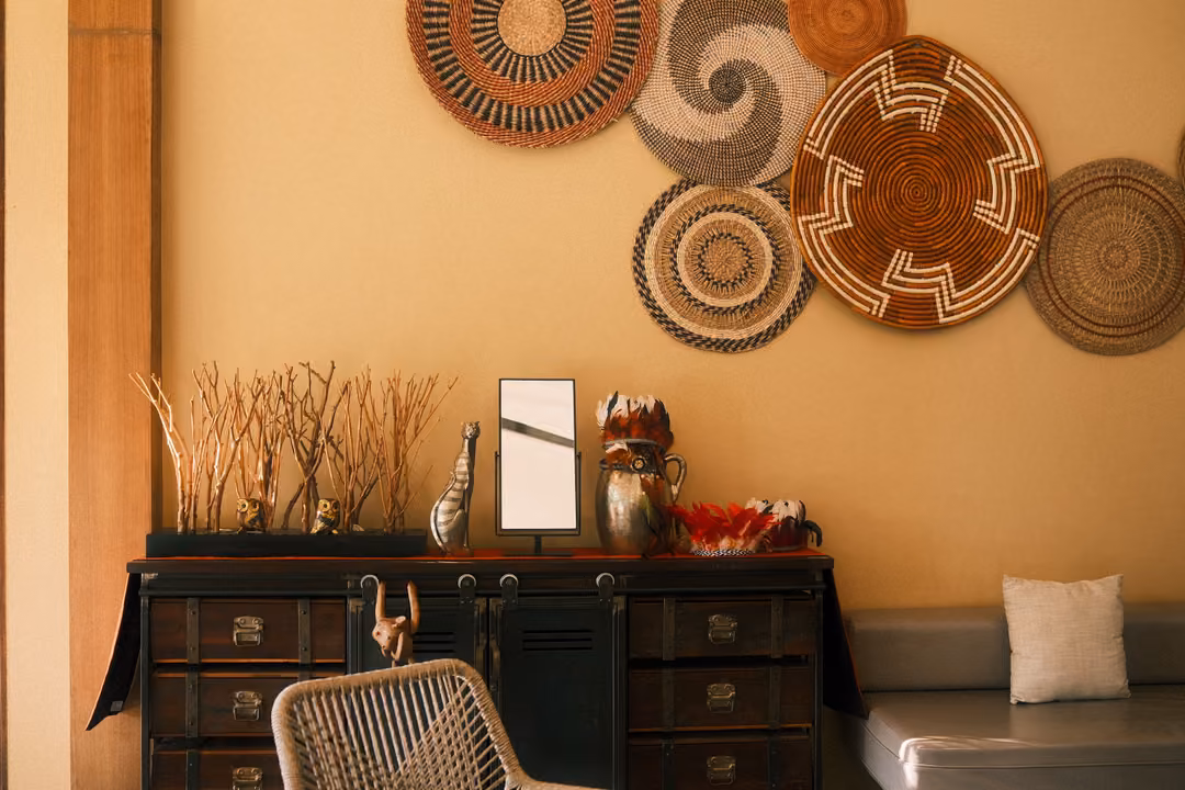 Woven baskets mounted on a warm yellow wall above a dark cabinet with dried branches, a mirror and vases