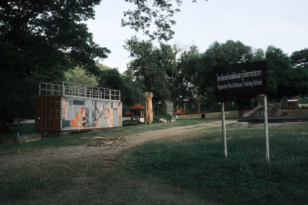 Black sign for a fire and rescue training school beside a painted container on a grassy field