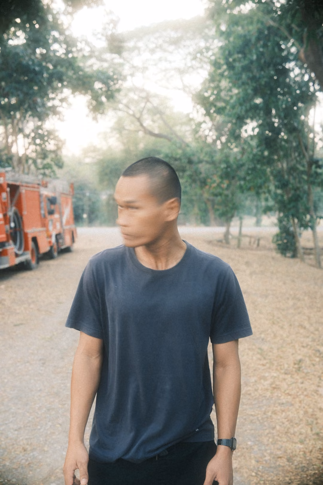 Man in a grey t-shirt turning his head sharply, face blurred, red fire vehicles parked behind on the road
