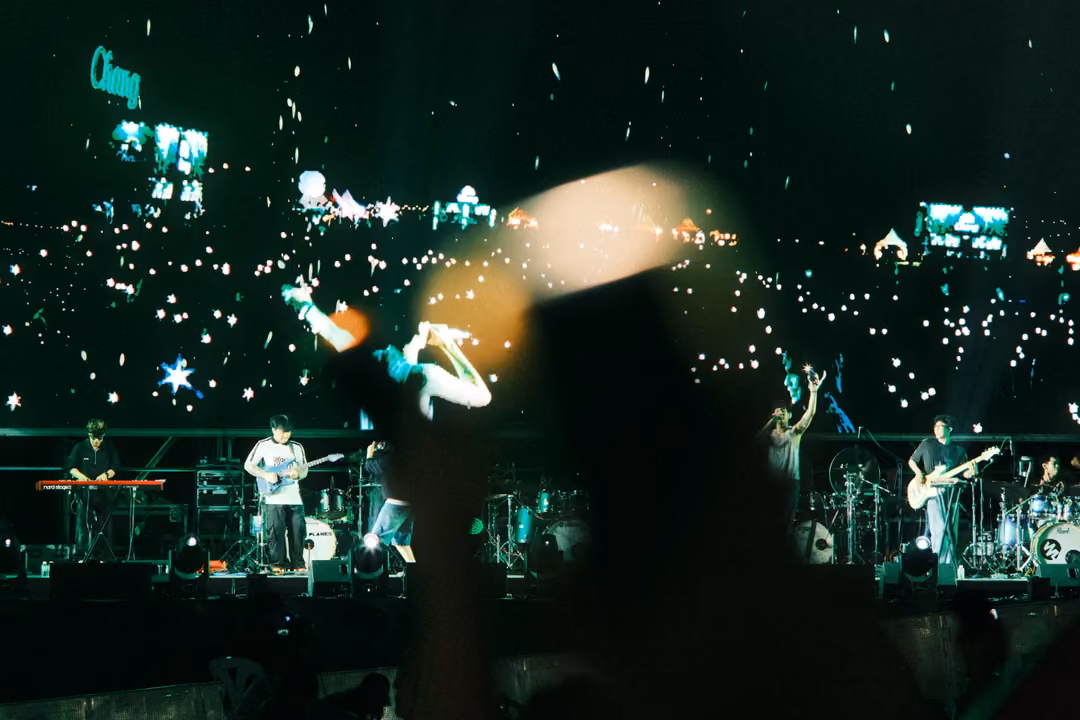 Screen showing a crowd's phone lights and a singer with arms outstretched, blurred raised hands in the foreground.