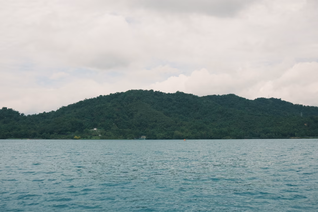 Rounded forested hill rising from a grey-green lake beneath a thick bank of cloud
