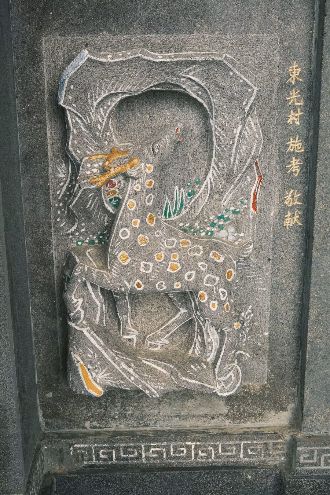Stone relief of a spotted deer with gold antlers in a carved frame, gold characters along one side