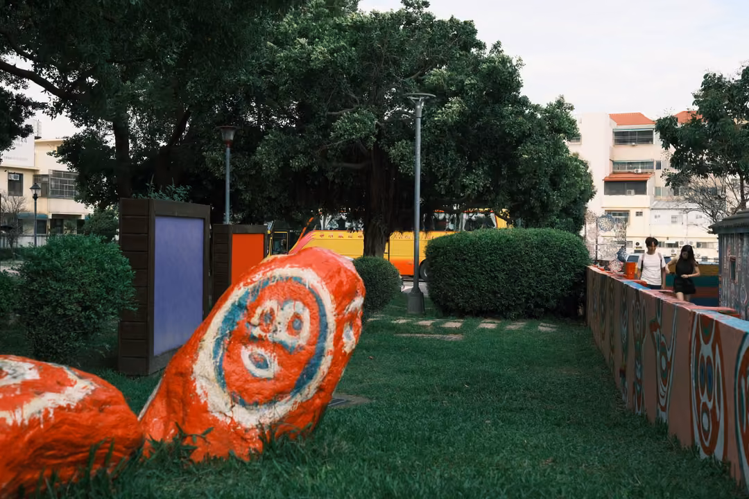 Painted orange boulders with large face designs on a lawn, painted walls and trees behind