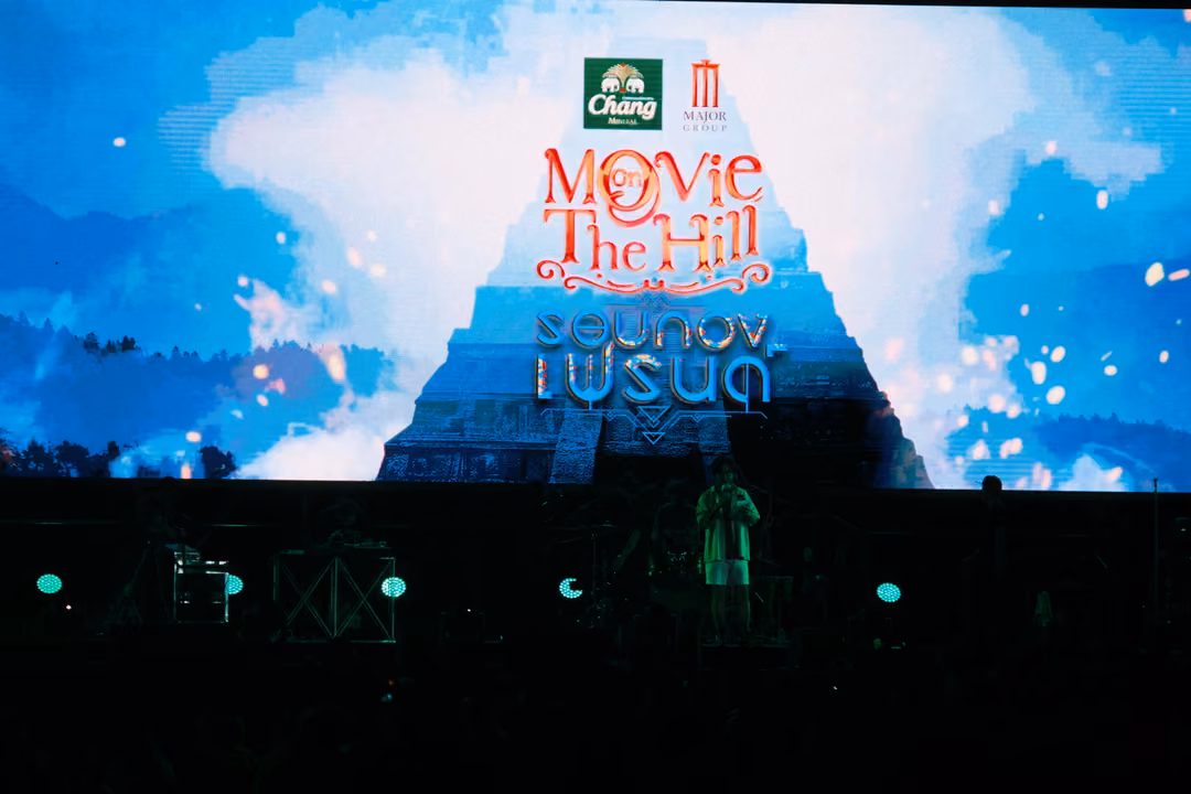 Big screen showing a Movie on The Hill logo over a blue sky with clouds and a stepped pyramid, stage dark below
