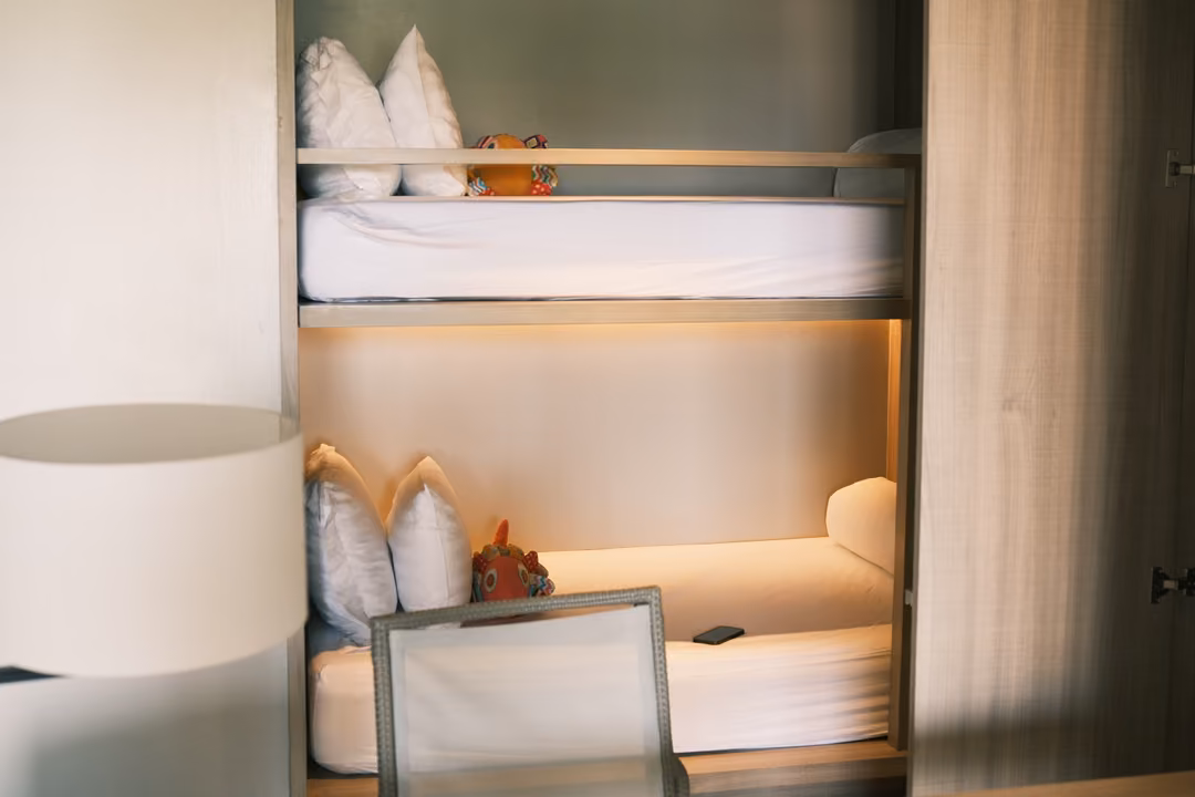 Built-in bunk beds with white bedding, cushions and a small soft toy, lit warmly from inside