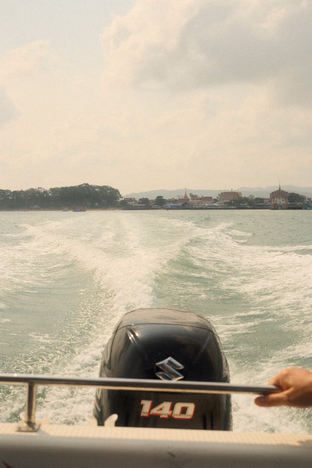 The same outboard motor and wake, with a hand gripping the stern rail on the right.