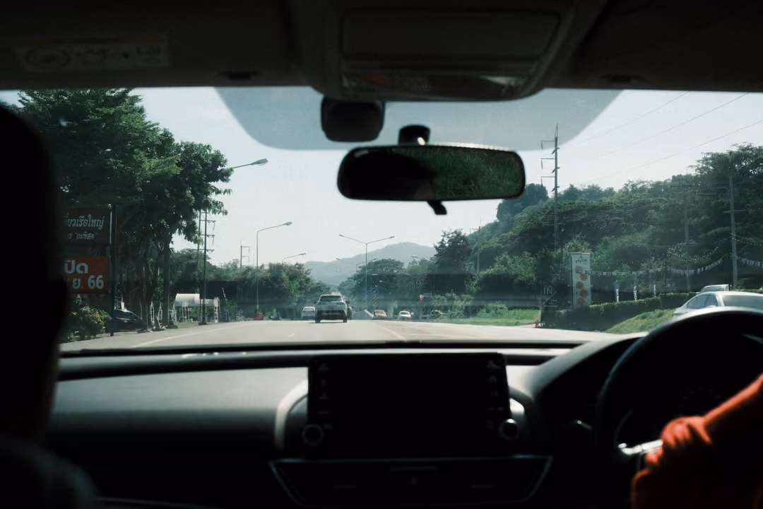 Windscreen view of a highway with roadside signs, hills ahead, the dashboard and a red sleeve in frame