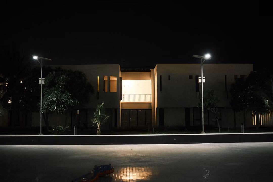 Two-storey villa at night with a lit upper balcony, street lamps and a dark pool in front