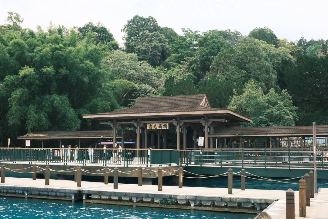 Closer view of the wooden pier pavilion and its railings, figures waiting under the roof, turquoise water