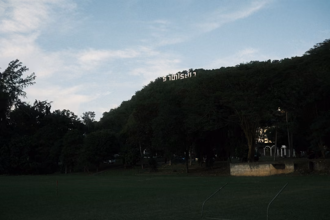Dark forested hill silhouetted against a blue sky with white letters on the ridge, a dark field below