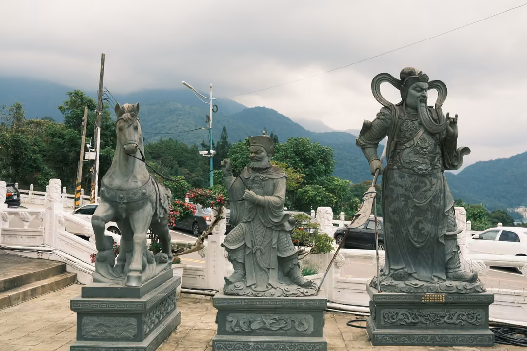 Three grey stone statues, a horse and two armoured figures, on plinths before misty mountains