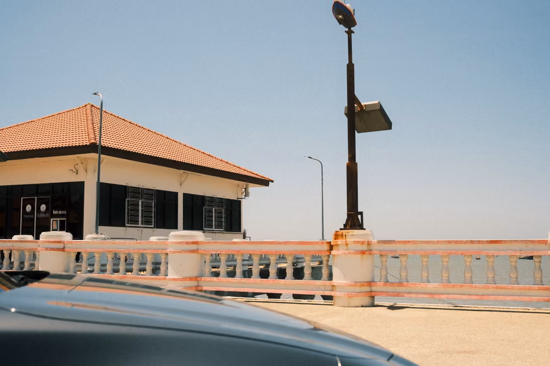 Seaside promenade with a white balustrade, an orange-roofed pavilion and a tall lamp post under clear sky