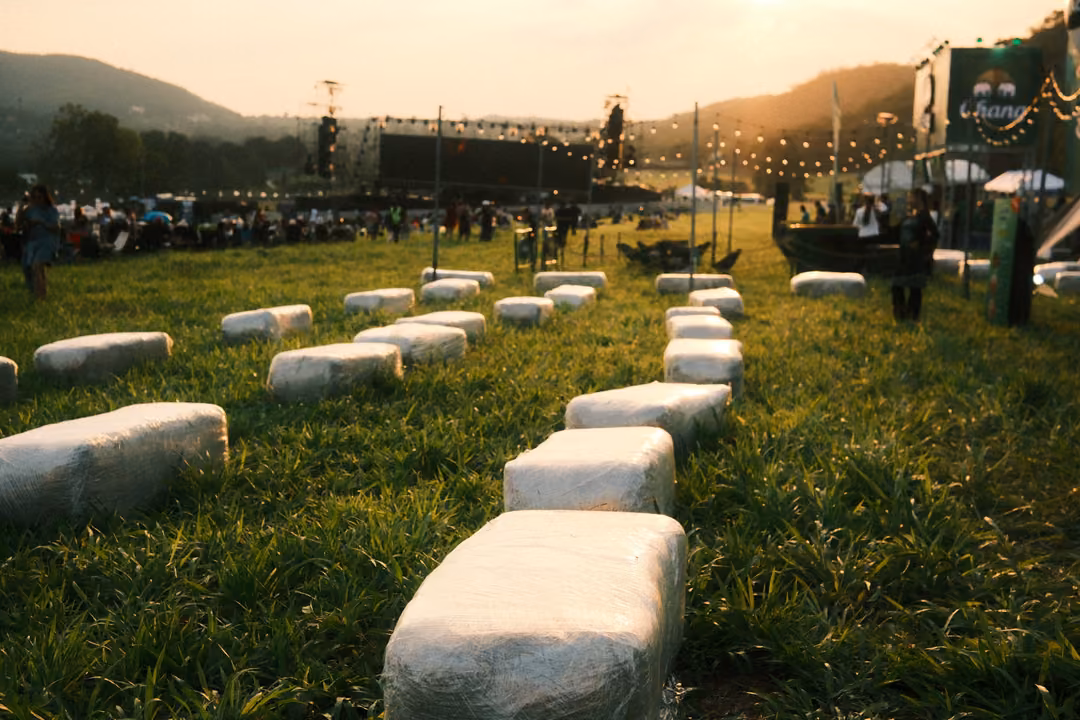 Rows of white-wrapped bales set out as seats on a grassy field, a stage and crowd behind.