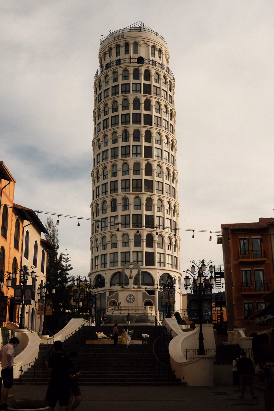 Tall cylindrical tower with rings of arched windows above a staircase, string lights and silhouetted visitors
