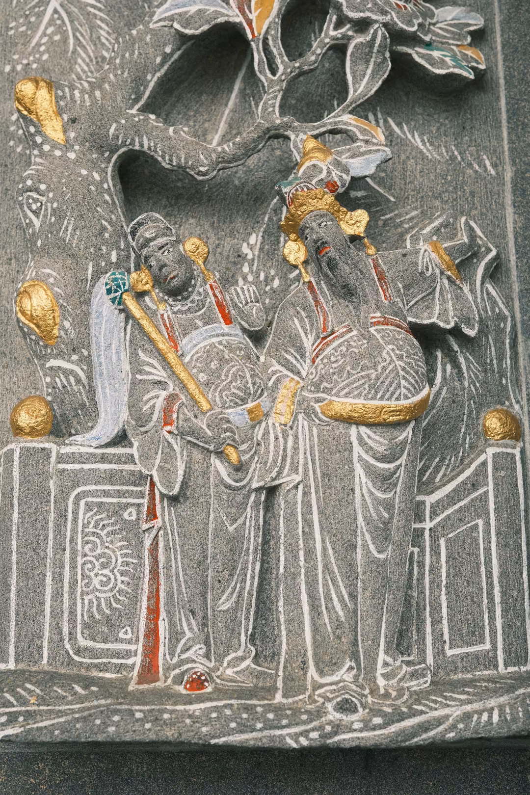 Tight crop of the carved stone figures in robes and gold crowns beneath the flowering branch