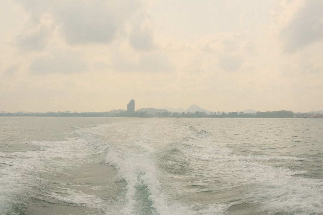 A straight wake running back to a faint shoreline, the tall tower small and centred on the horizon.