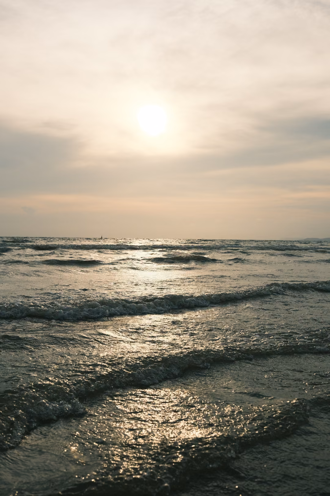 Waves rolling toward the shore under a hazy sun, light reflecting on the water