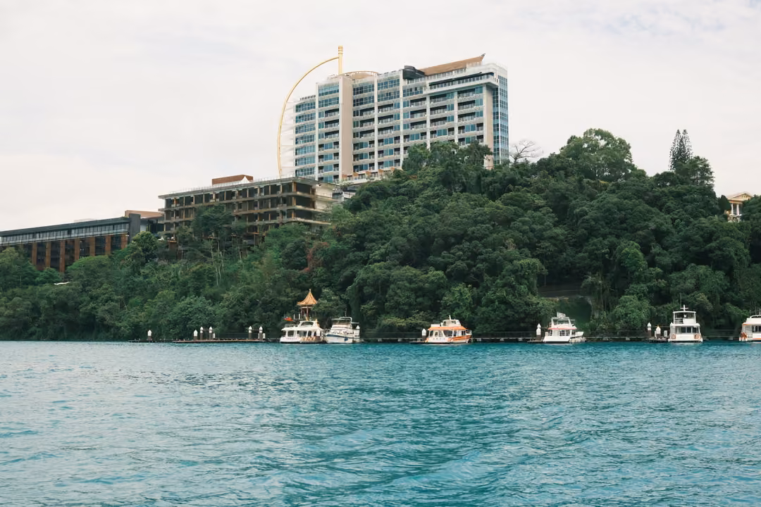 Same turquoise lakeshore, forest and tower, framed slightly lower with boats along the waterline
