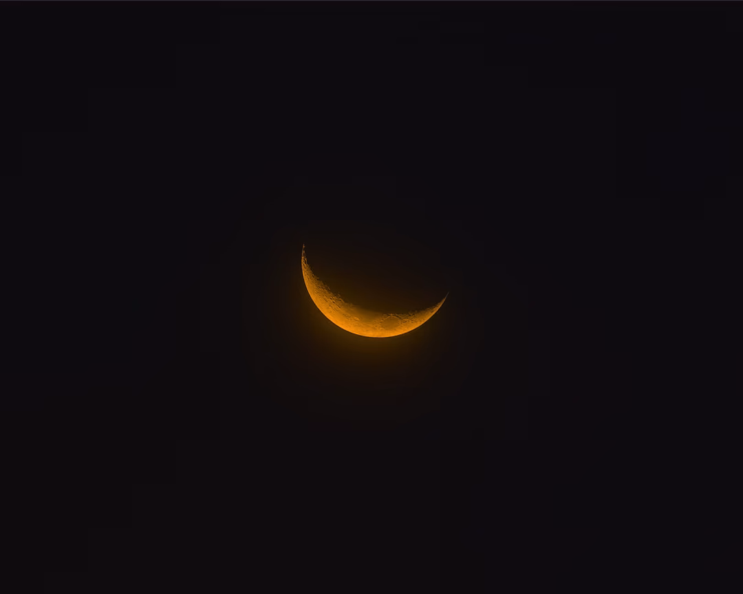 A thin orange crescent moon glowing against a near-black sky