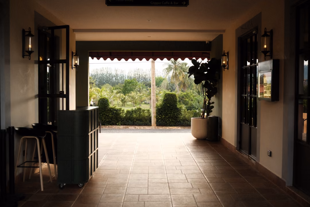 Covered tiled passage with wall lanterns opening onto a bright view of green trees and hedges