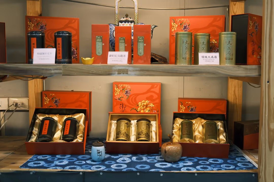Same red tea gift display with tins on satin and a small blue pot on the cloth, viewed slightly to the right