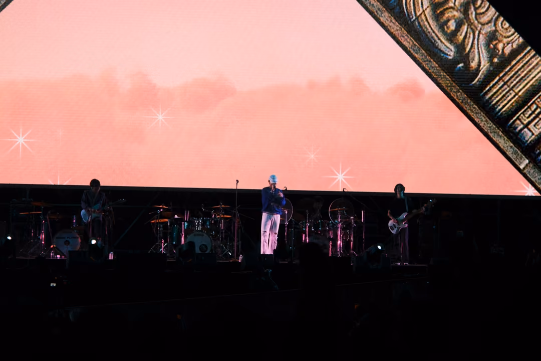 Stage with a pale pink cloud screen sparkling with stars, the singer at a microphone stand and two guitarists below.