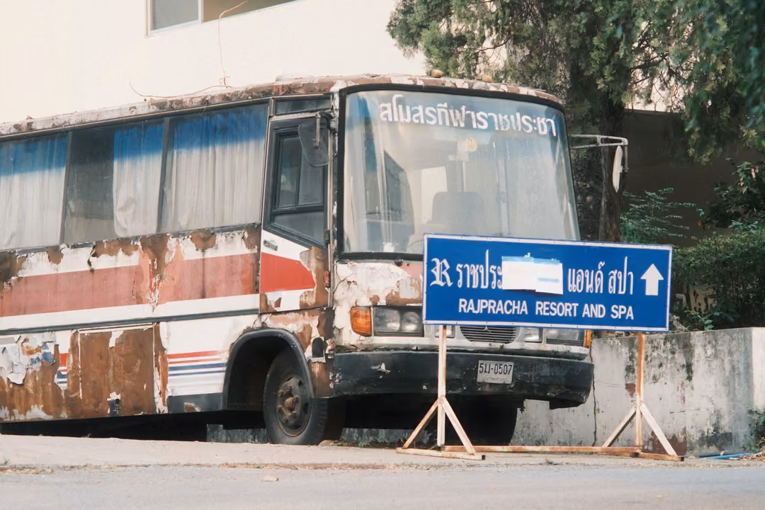 Old rust-streaked bus parked behind a blue sign with an arrow pointing to a resort and spa