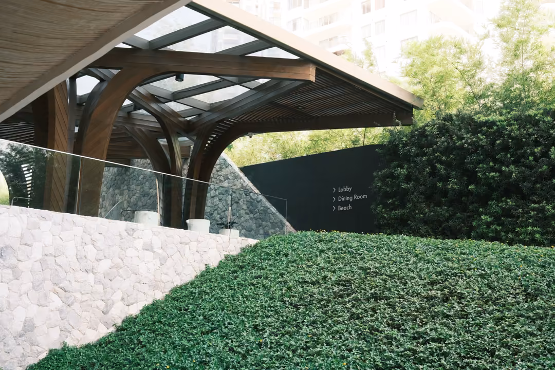 A curved wooden canopy over a stone wall and sloping lawn, a sign listing Lobby, Dining Room, Beach