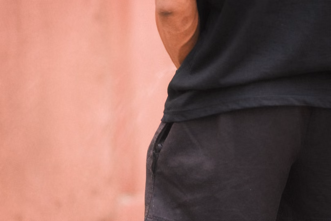 Tight crop of a person's torso in black shirt and shorts standing beside a soft pink wall