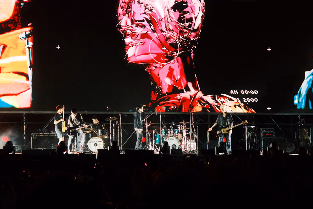 Giant screen showing a red and magenta chrome head over a dimly lit band; the crowd has fallen into near darkness