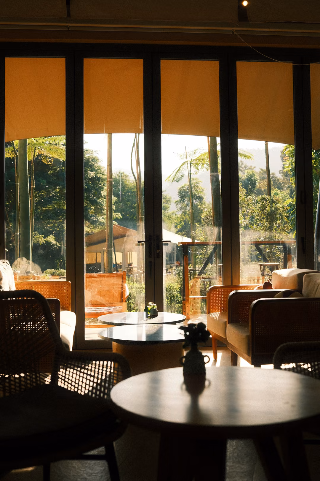 Dark round table with a small vase in silhouette, tall bright windows and lounge chairs behind